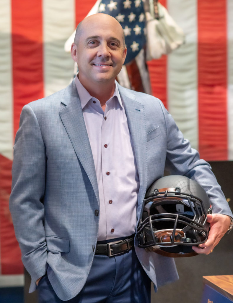 Brian Carlock smiling while holding a football helmet