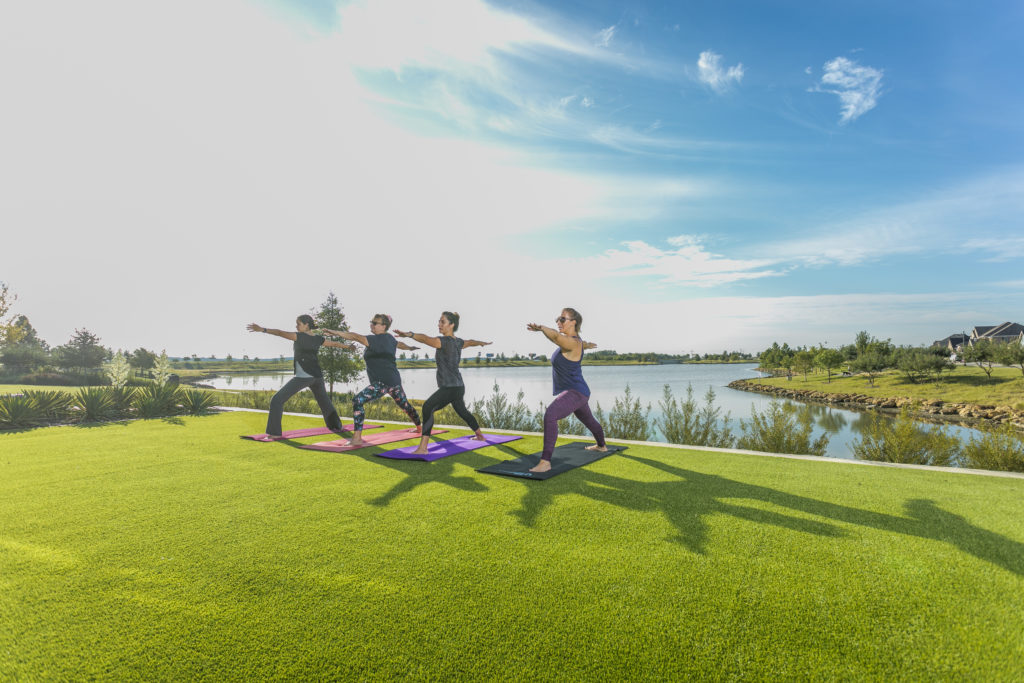 Four women practicing yoga on the grass overlooking a lake at a Lifestyle by Hillwood community