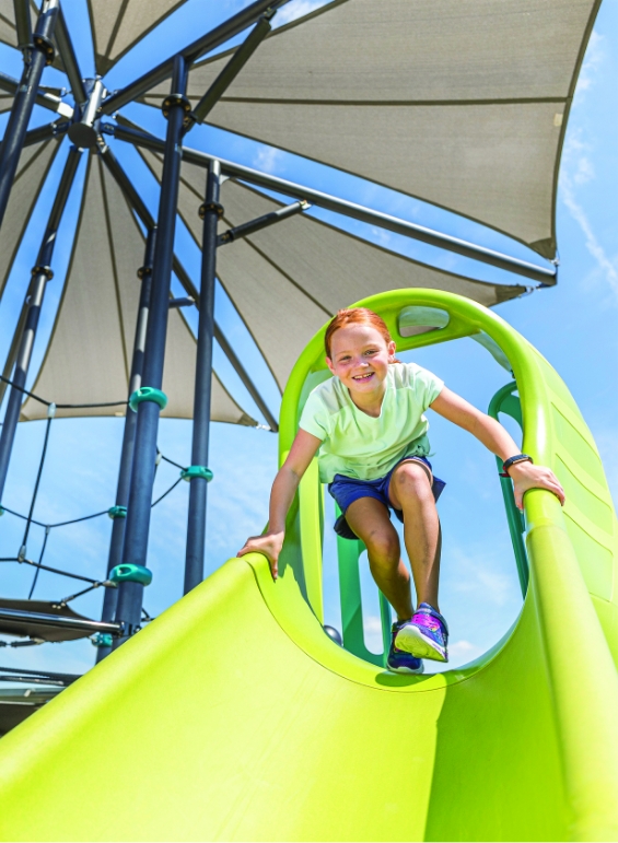 A young girl playing on a bright green slide at a Lilyana park