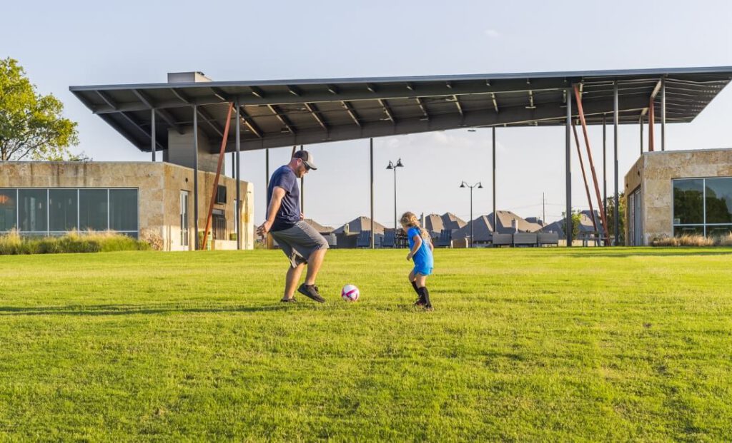 A father playing soccer with his daughter in a field in their local Lifestyle by Hillwood community