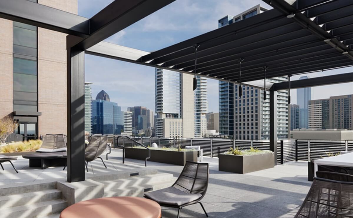 A rooftop terrace with chairs, tables and plantings overlooking the Dallas skyline