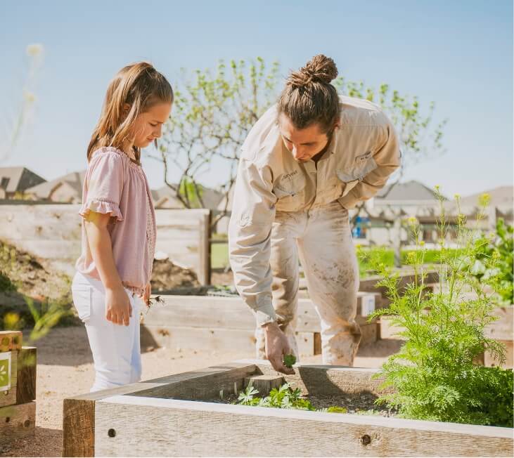 A father helping his daughter plant vegetables at a community garden