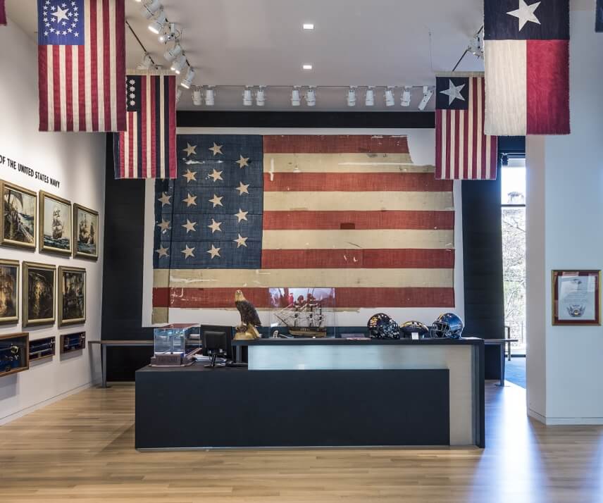 A room in the Hillwood Headquarters building with a large American flag as well as previous versions of the American and Texas flags.