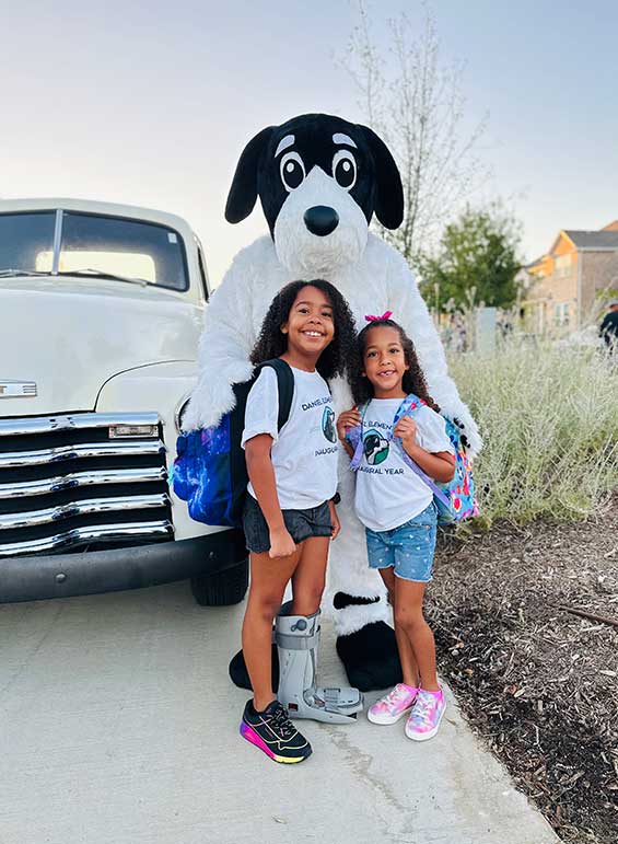 Two schoolchildren standing in front of a school mascot