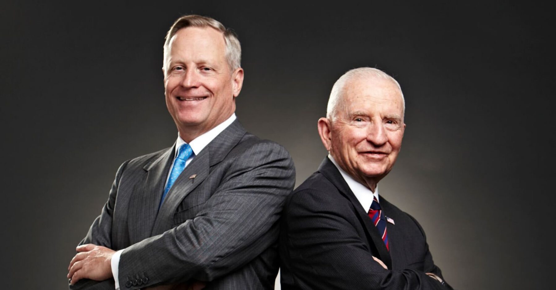 Ross Perot Jr. and Ross Perot Sr. standing back-to-back and smiling.