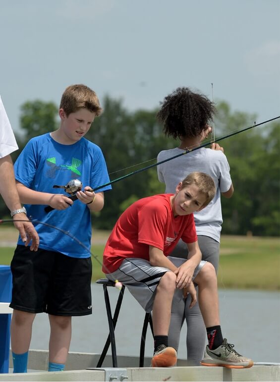 Three kids fishing off the dock at the lake at Pomona