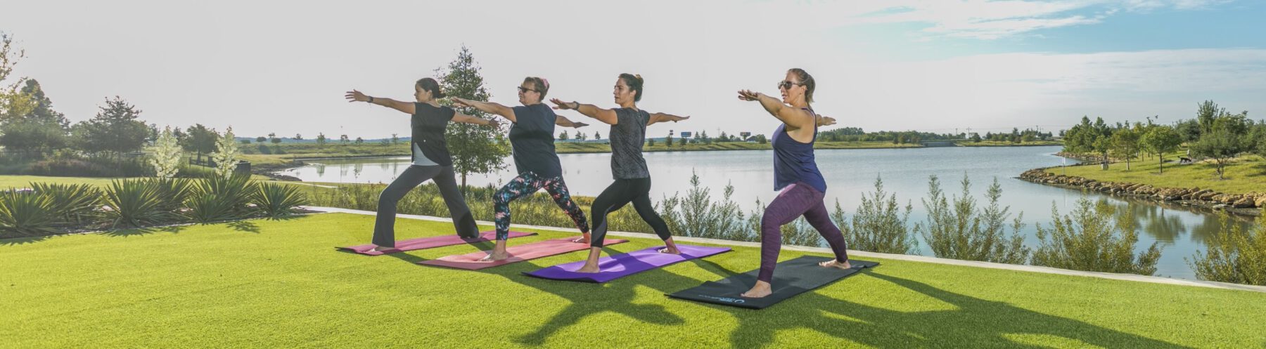 Four women practicing yoga on the grass overlooking a lake at a Lifestyle by Hillwood community