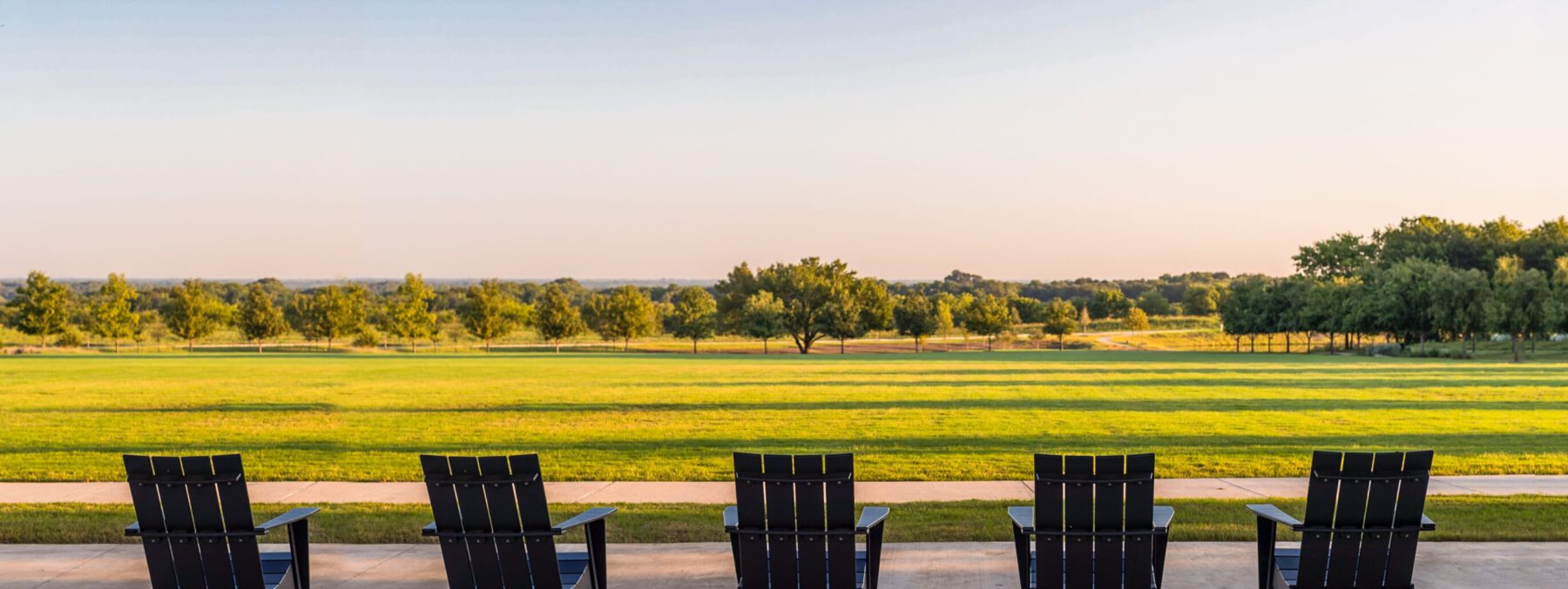Lawn chairs overlooking the Texas landscape at sunset, with a lawn of green grass and trees in the background