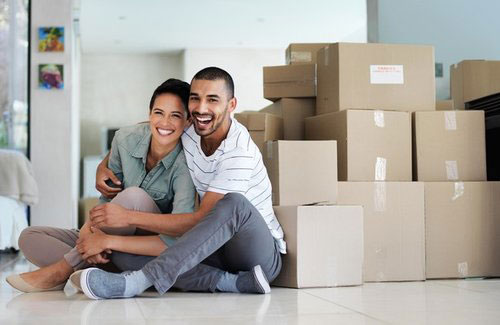 A young couple smiling in front of moving boxes