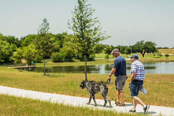Two men walking with a dog along a path in a Lifestyle by Hillwood community