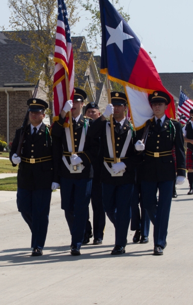 Military members carrying the American and Texas flags during a parade through Harvest