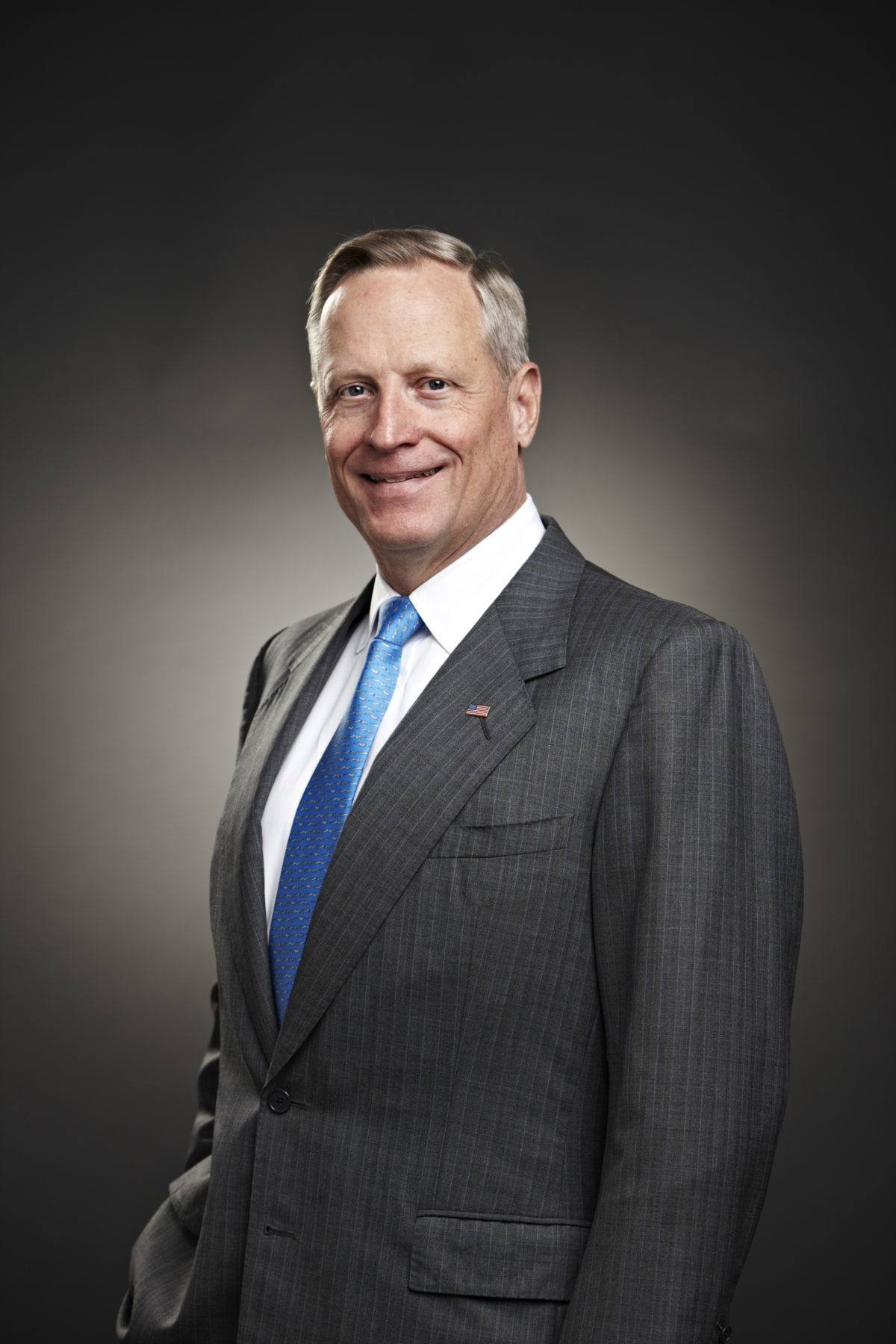 A headshot of Ross Perot Jr. smiling and wearing the grey suit and blue tie