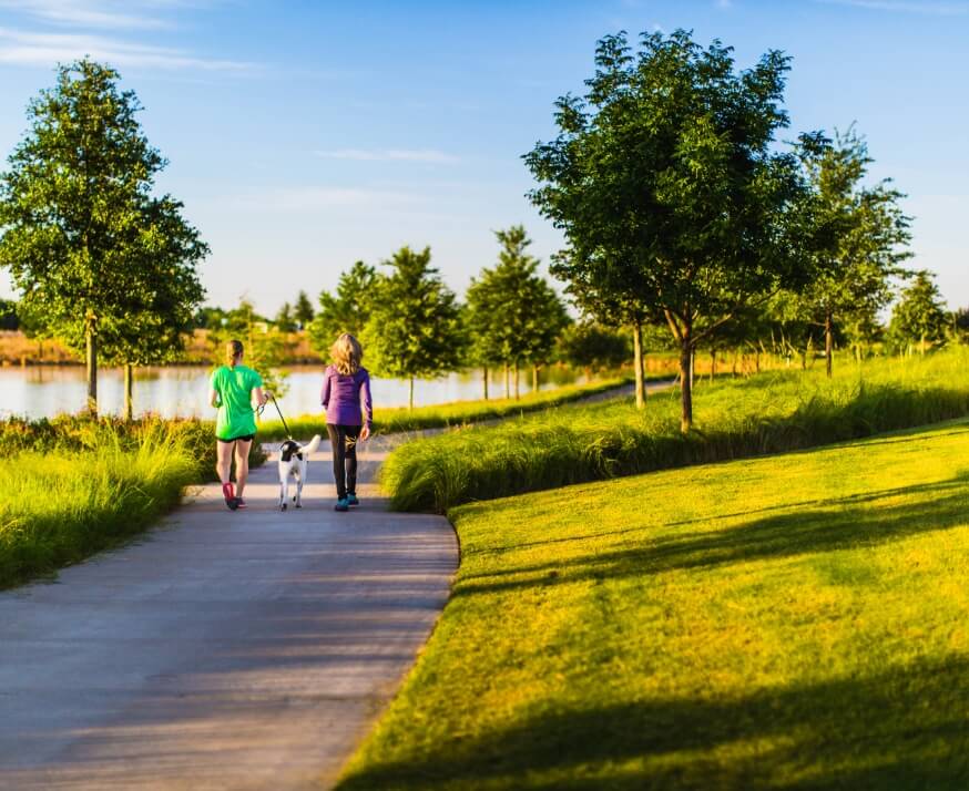 Two women walking their dog on a trail at a Lifestyle by Hillwood community