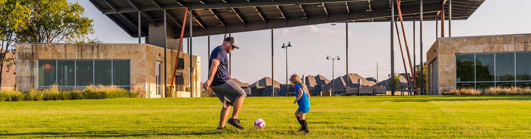 A father and daughter playing soccer in a park at a Hillwood community