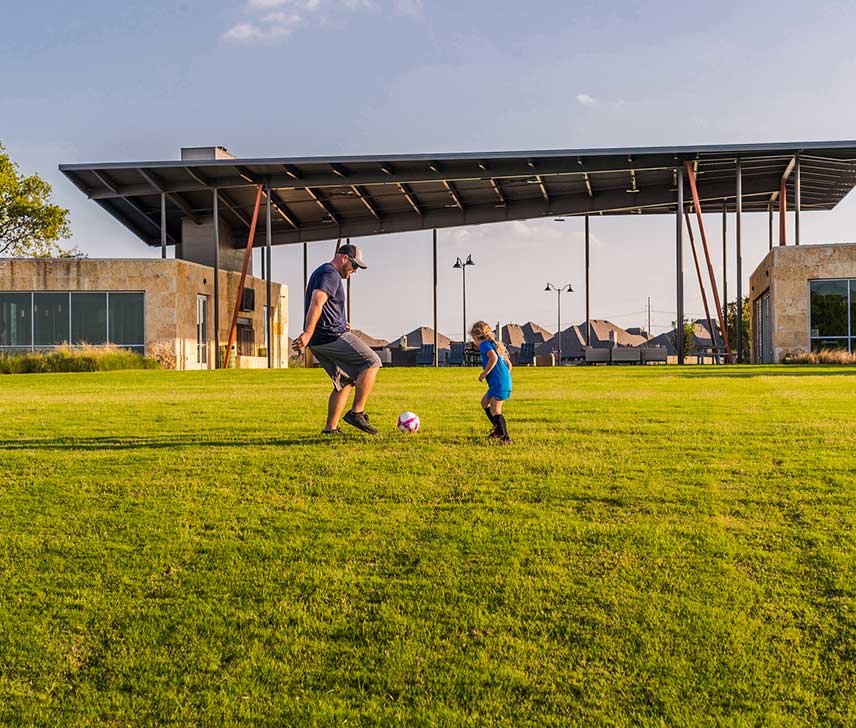 A father and daughter playing soccer in a park at a Hillwood community