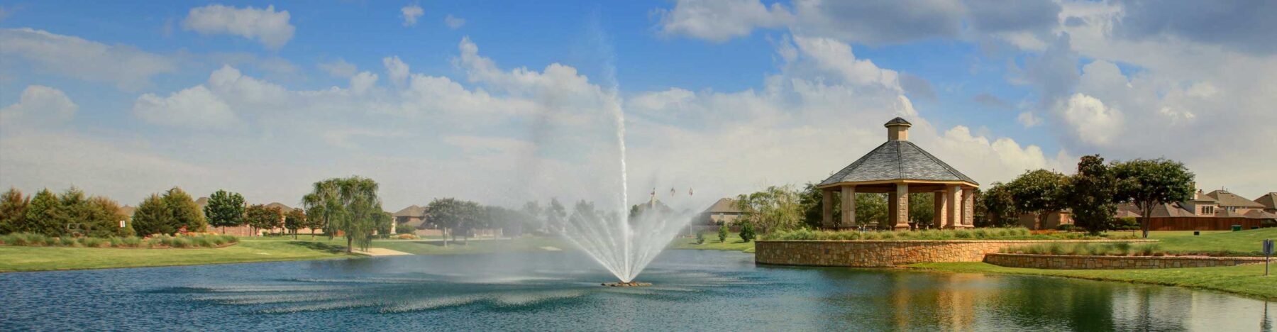 A fountain and pond with a nearby gazebo in a Hillwood community