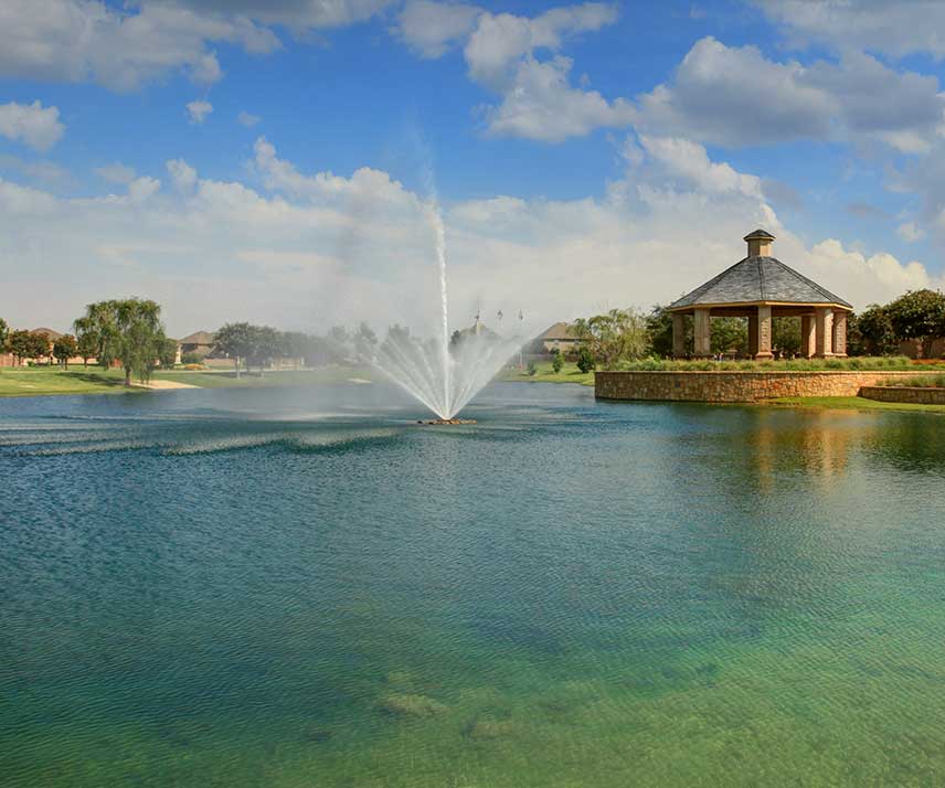 A fountain and pond with a nearby gazebo in a Hillwood community